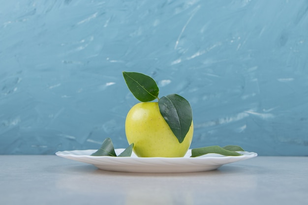 Single apple with leaves on white plate. 