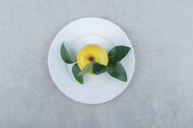 Single apple with leaves on white plate. 