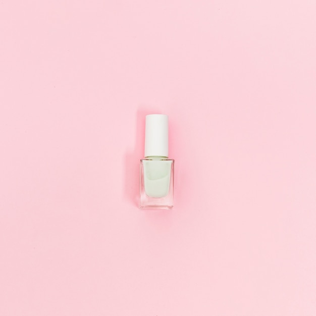 Single bottle of white nail polish on pink background