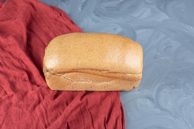 Free photo single bread loaf on a red tablecloth on marble surface.