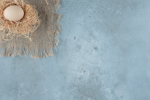 A single egg on a small pile of straw on marble background. High quality photo