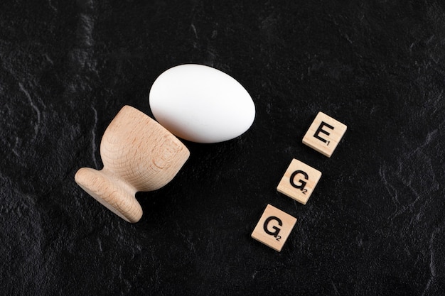 Single egg and wooden letter spelled as egg on black surface. 