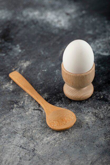 Single egg and wooden spoon on marble surface. 