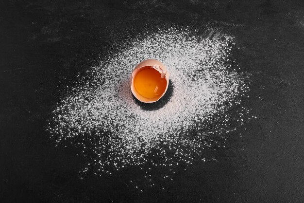 Single eggshell on flour on black surface. 