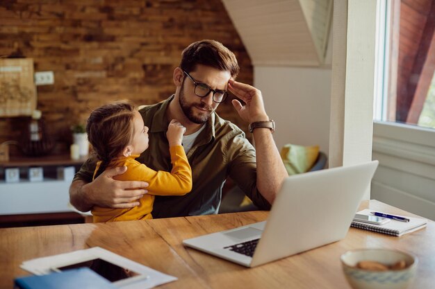 Single father reading problematic email on laptop while working at home