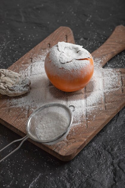 Single fresh persimmon fruit with flour on wooden board