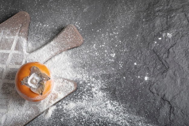 Free photo single fresh persimmon fruit with flour on wooden board