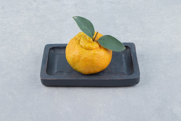 Бесплатное фото Один свежий мандарин с листьями на черной тарелке.