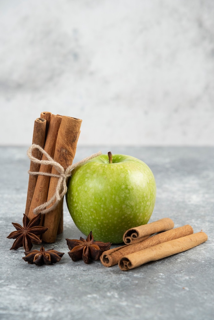 Free Photo single green apple and cinnamon sticks on marble table.