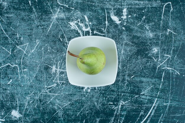 Single green pear in white bowl. 