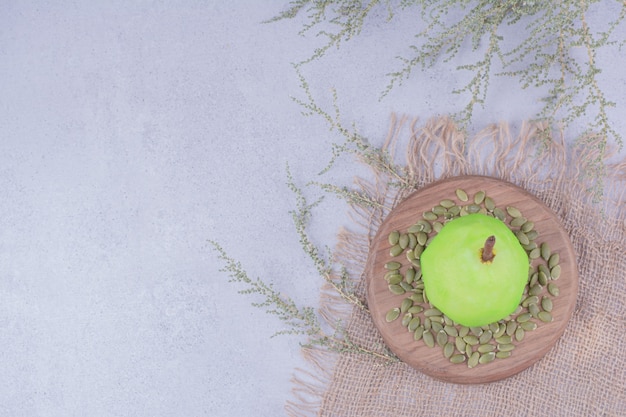 A single green pear on a wooden board with pumpkin seeds around