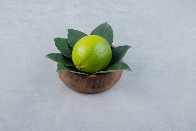 Single lime with leaves in wooden bowl. 