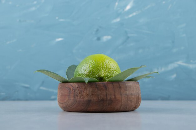 Single lime with leaves in wooden bowl