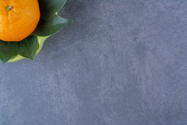 A single orange with leaves in bowlon marble table.