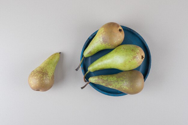 A single pear next to a bundle of pears on a platter on marble 