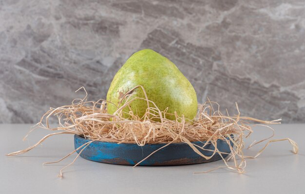 A single pear on a straw pile in a small blue platter on marble 