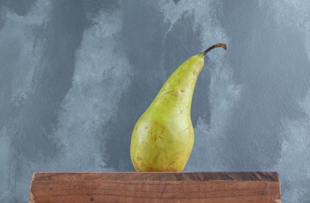 A single pear on a wooden board on marble 