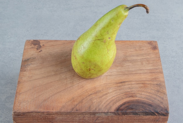 Free photo a single pear on a wooden board on marble
