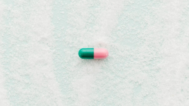 Single pink and green capsules on salt background