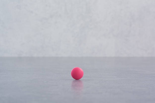 Single pink pill on marble table.