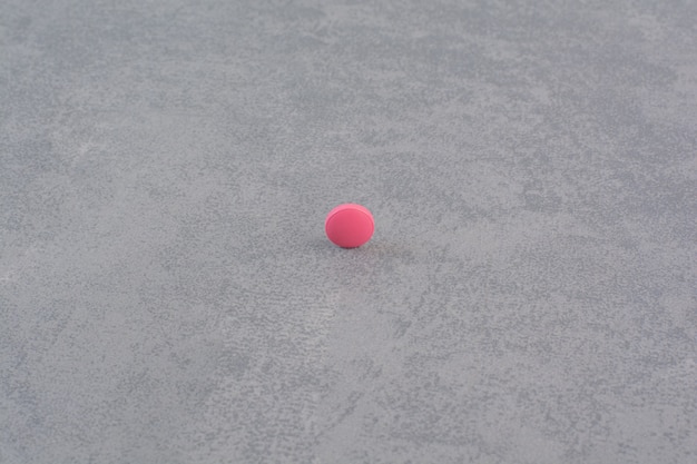 Single pink pill on marble table.