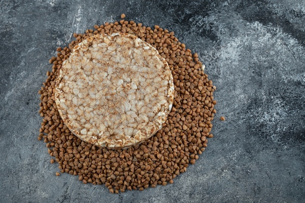 Одиночный рисовый пирог и сырая гречка на мраморной поверхности