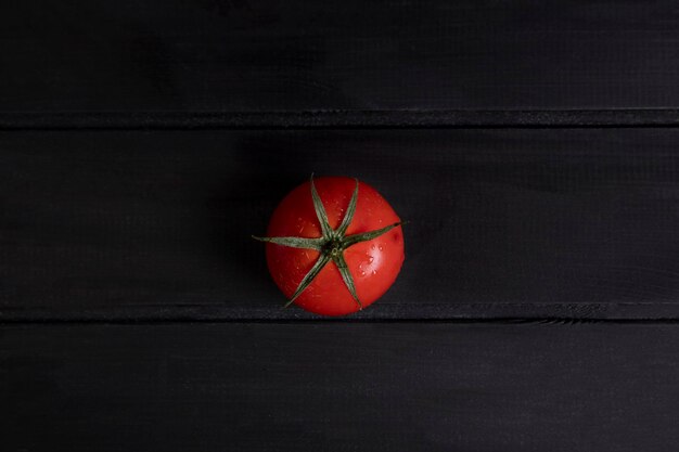 Single ripe red tomato placed on dark wooden surface. High quality photo