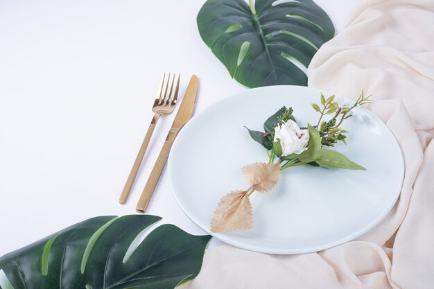 가짜 잎과 식탁보와 흰색 접시에 단일 로즈.
