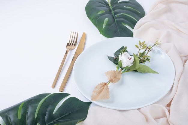 Single rose on white plate with fake leaves and tablecloth.