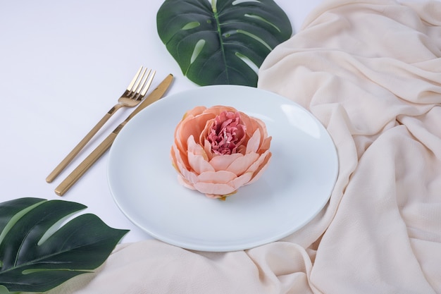 Free photo single rose on white plate with fake leaves and tablecloth.