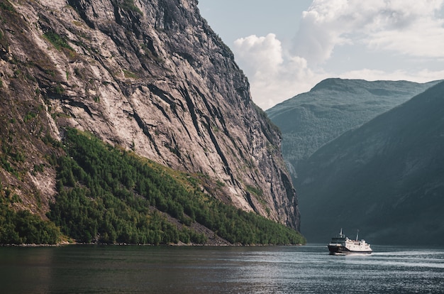 ノルウェーの曇り空の下で高い岩山に囲まれた湖で1隻の船
