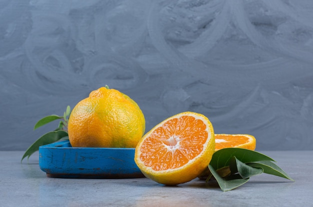 Foto gratuita mandarino singolo su un piatto accanto a mandarini a fette con foglie su sfondo di marmo.