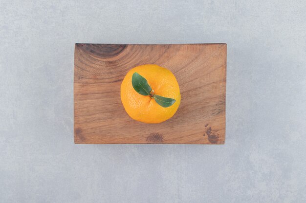 Single tasty clementine on wooden board. 