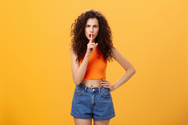 Sister displeased sibling saying cursing words standing serious and strict over orange background in...