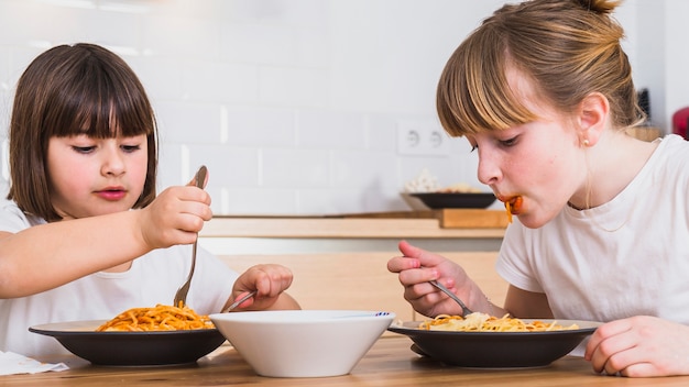 Sorelle che mangiano pasta deliziosa in cucina