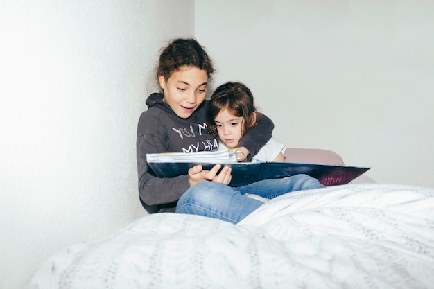 Sisters reading magazine in bed