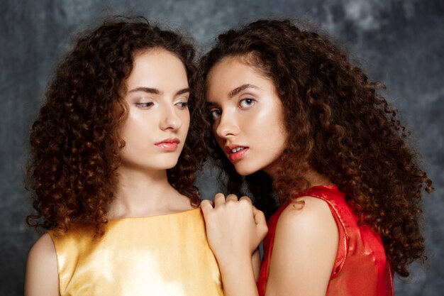 sisters twins posing smiling on grey