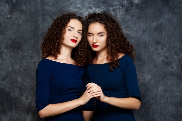 Sisters twins smiling winking on grey