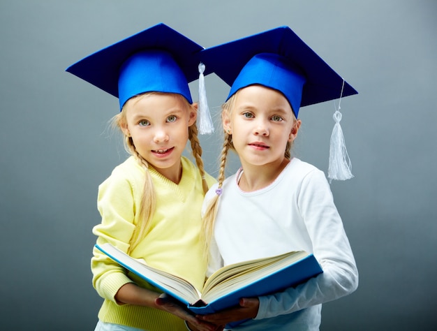 Foto gratuita sorelle con tappi di laurea che condividono un libro