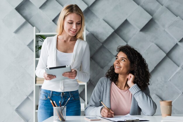 Sitting at desk ethnic woman and standing blond coworker