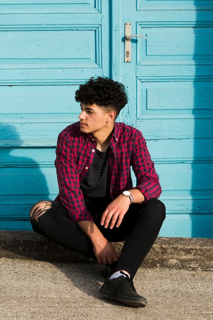 Free photo sitting ethnic teenager in checkered shirt on curb