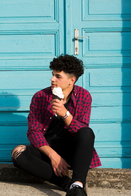 Free photo sitting ethnic youngster holding ice cream in checkered shirt