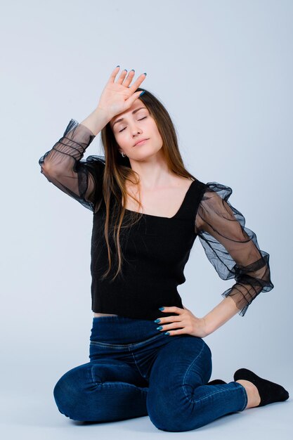 Sitting on floor girl is holding hand on forehead on white background