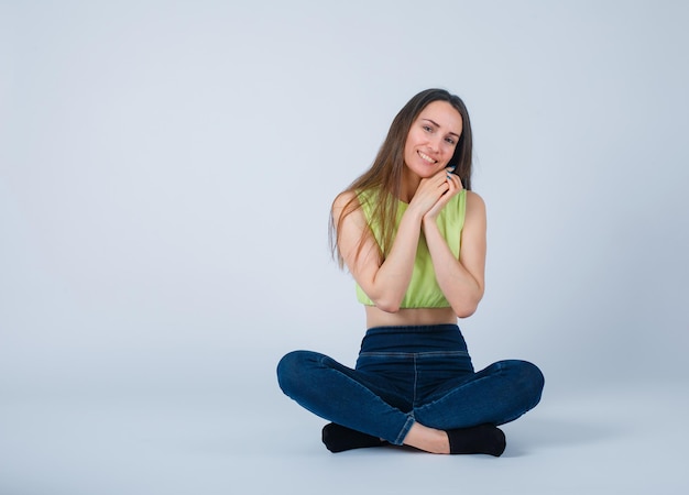 Free photo sitting on floor girl is looking at camera by holdin hands on chest on white background