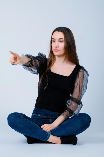 Sitting on floor girl is pointing away with forefinger on white background
