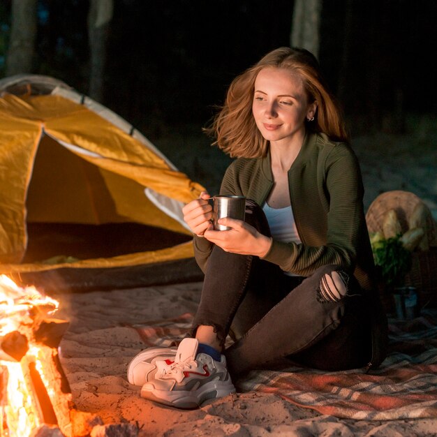 Sitting girl drinking by a campfire