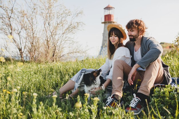 Sitting in grass, young stylish hipster couple in love with dog in countryside