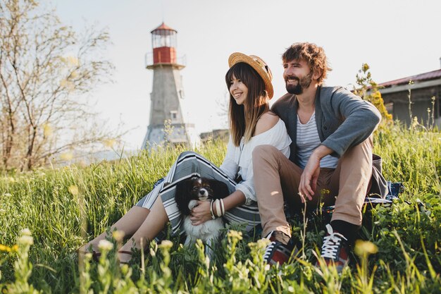 Sitting in grass, young stylish hipster couple in love with dog in countryside