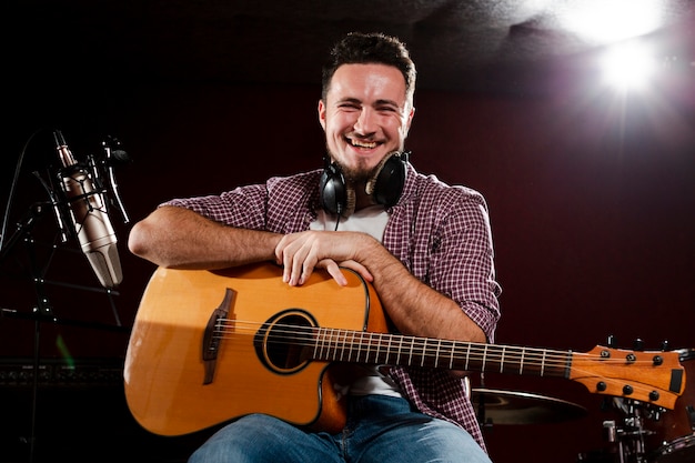 Foto gratuita uomo seduto in possesso di una chitarra e sorrisi