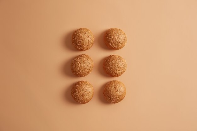 Six sesame burger buns arranged in two rows on beige studio background. Homemade brioche used as dinner rolls. Bread cooked at home by chef. Delicious food for breakfast. Overhead high angle view